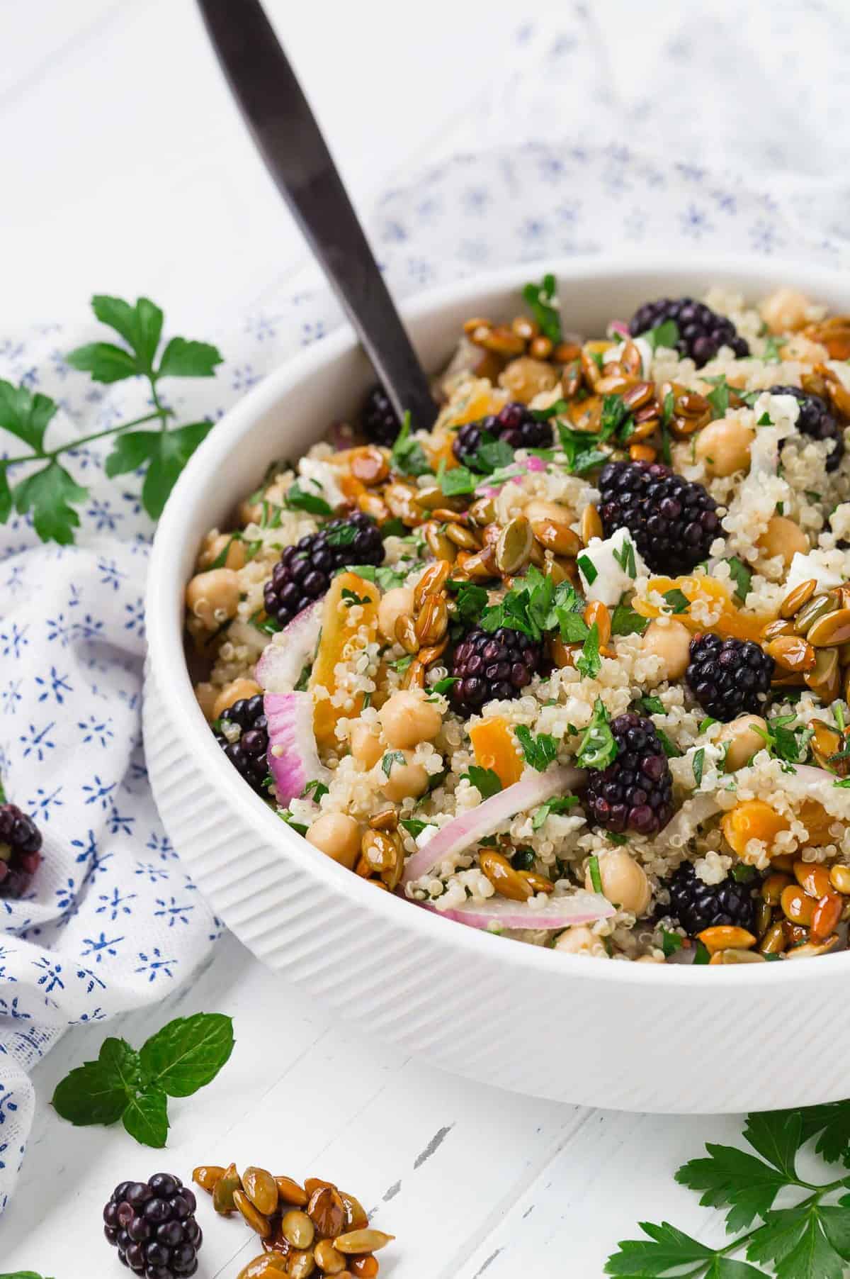 Hearty quinoa salad in a white bowl with a black spoon.