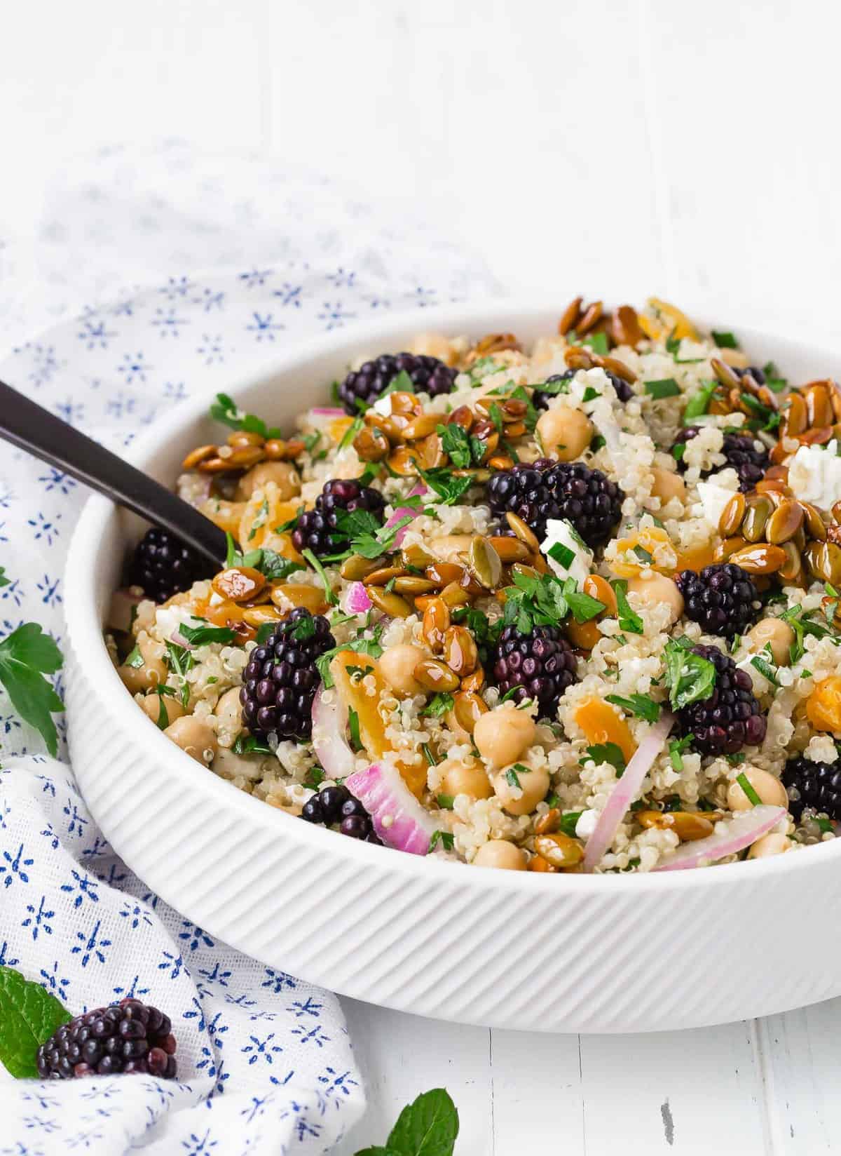 Colorful quinoa salad in a white bowl with a black spoon.