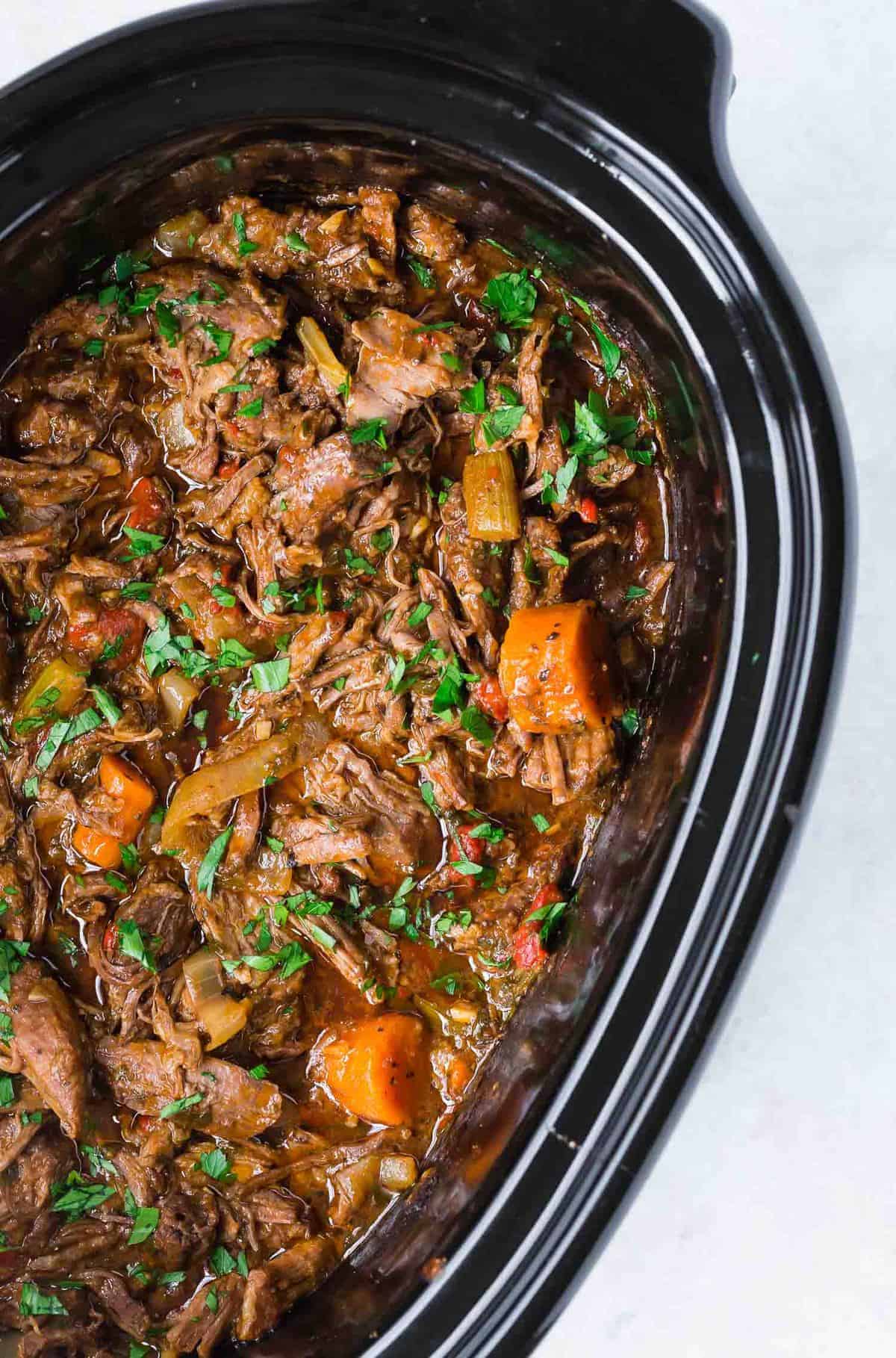 Pot roast and carrots in a black slow cooker.