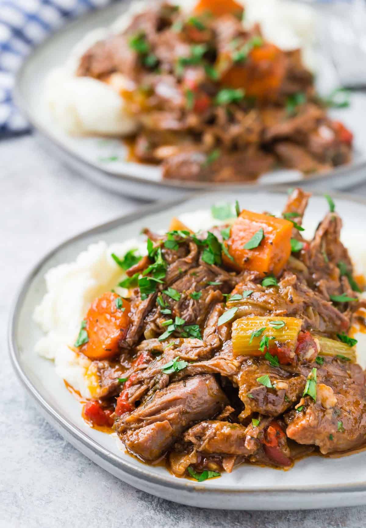 Close up of shredded pot roast on mashed potatoes, garnished with fresh parsley.