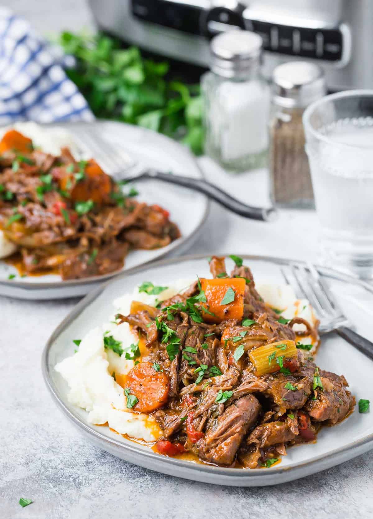 Pot roast on two plates, a slow cooker and salt and pepper shakers in the background.