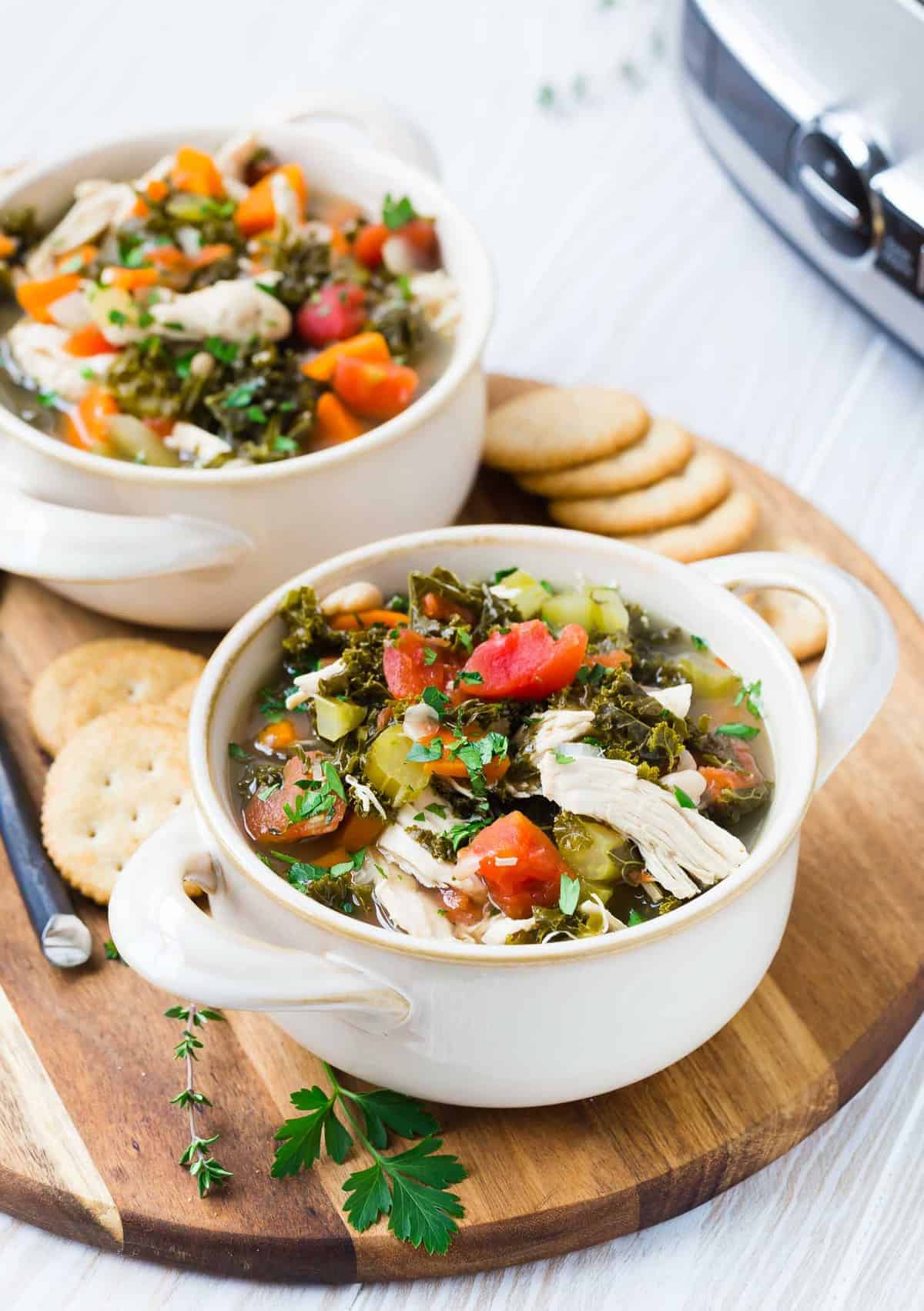 Two white bowls full of chicken and kale soup, garnished with fresh parsley.