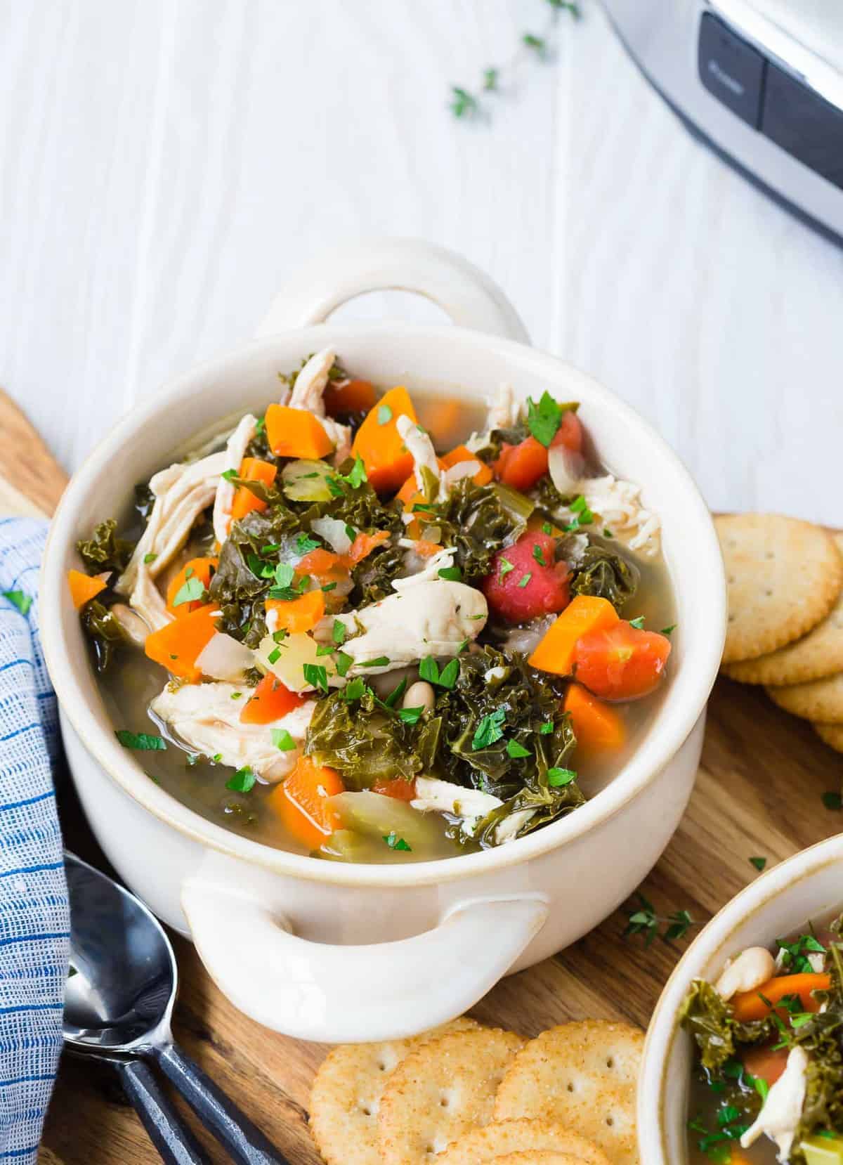 Kale, chicken, tomato, and carrot soup in a white bowl. 