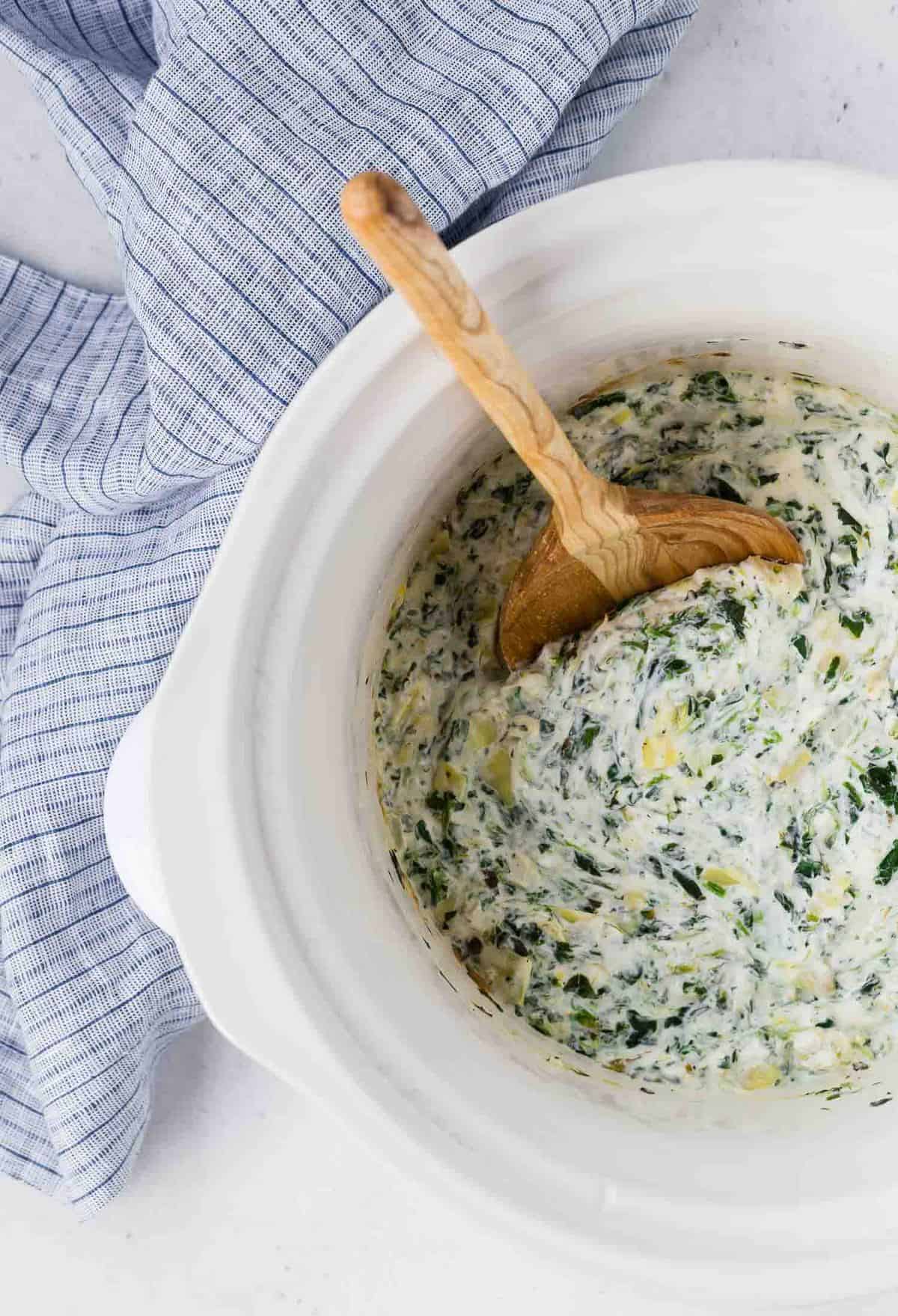 Overhead view of spinach artichoke dip in a white slow cooker.