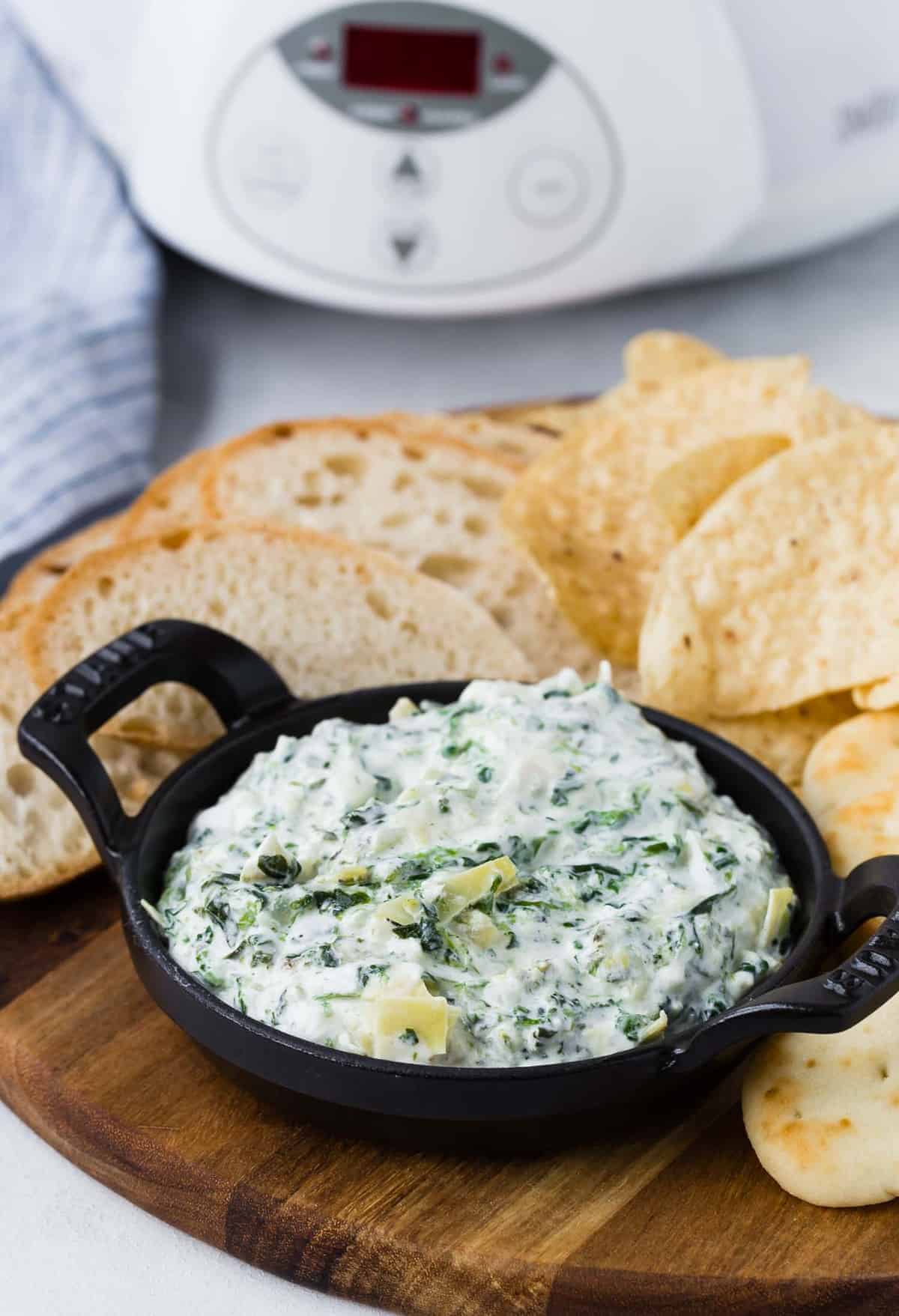 Small black bowl of dip on a wooden board with chips and bread.