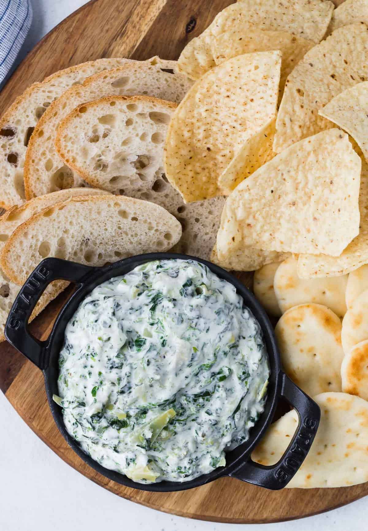 Overhead view of a small black dish of dip made with spinach and artichokes, surrounded by chips and bread.