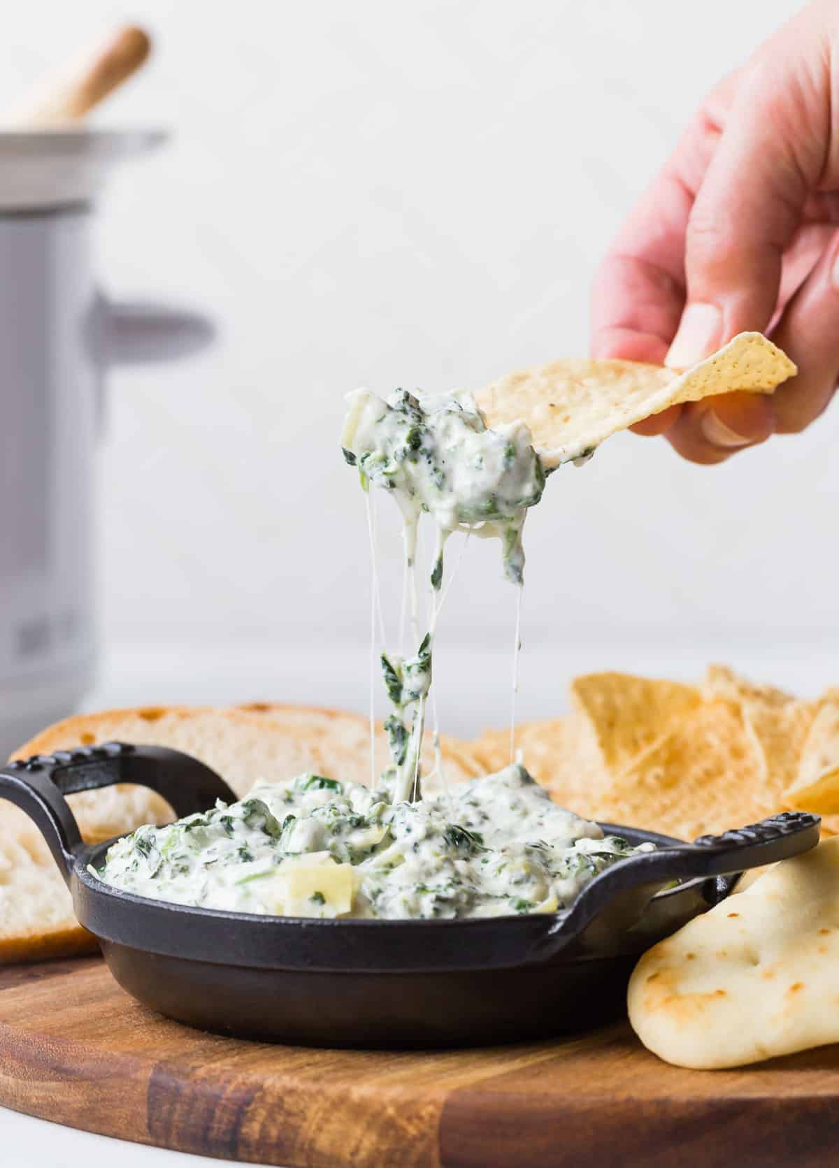 Chip being pulled up from a dish of spinach dip. 