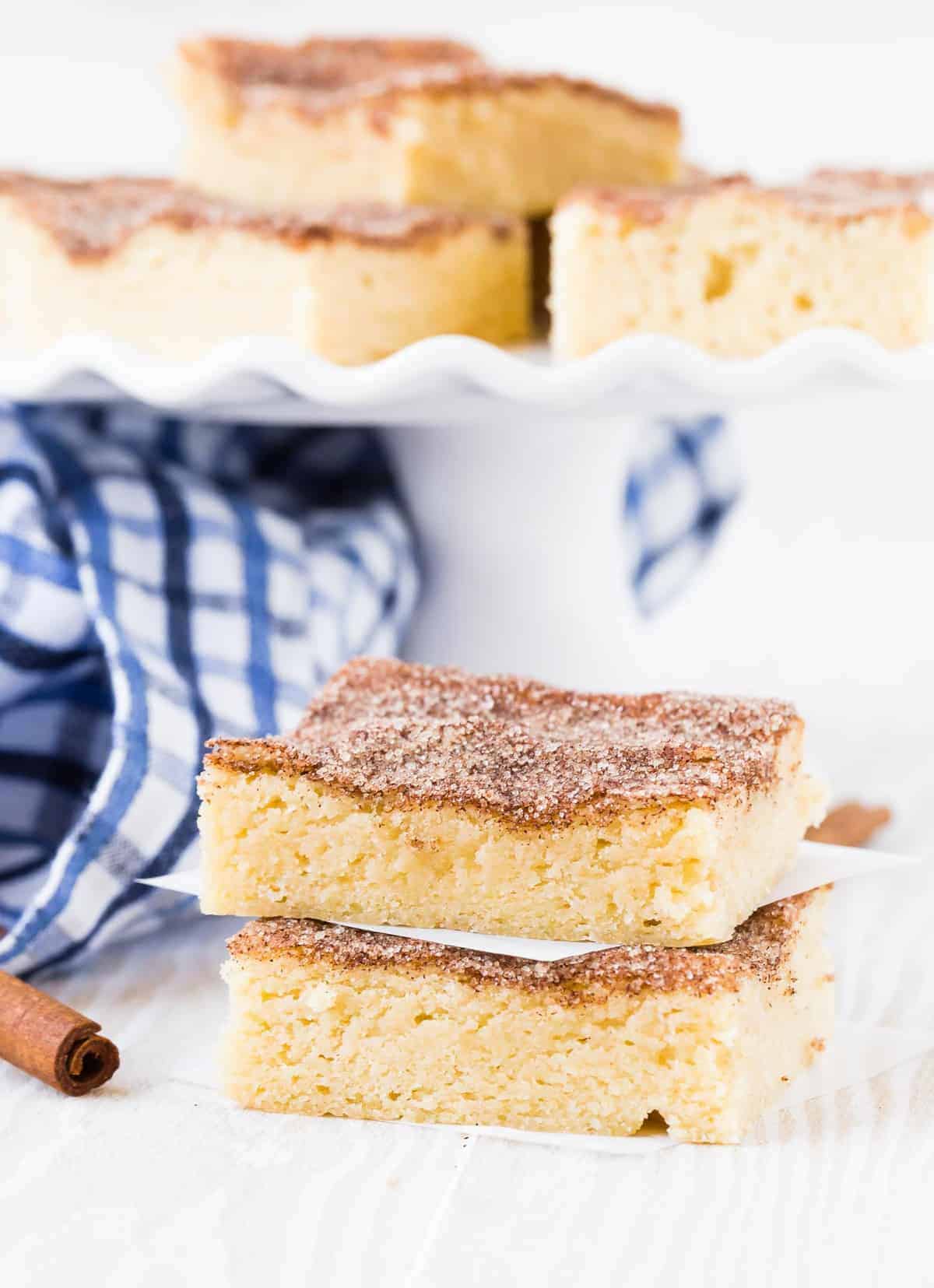 Two cinnamon sugar topped bars sitting in front of a small cake stand with more bars.