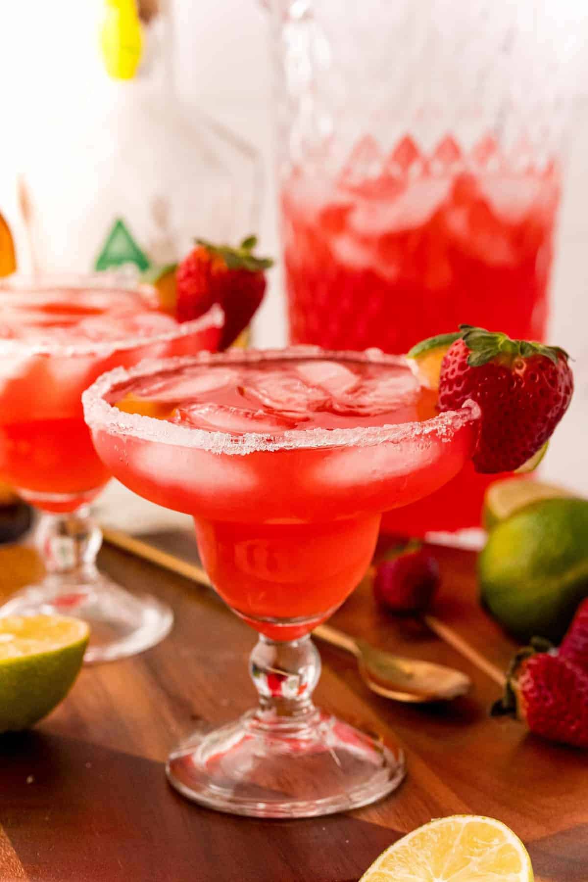 Strawberry margarita punch in a margarita glass in front of a pitcher.