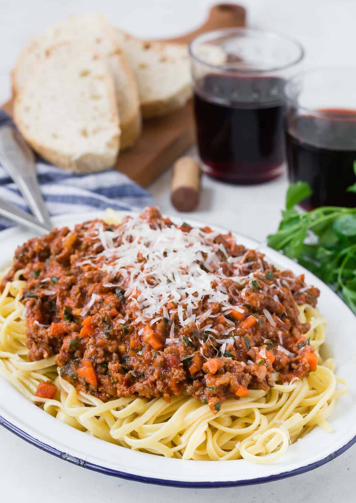 Large platter of pasta with tomato sauce, in front of wine, bread, and fresh herbs.