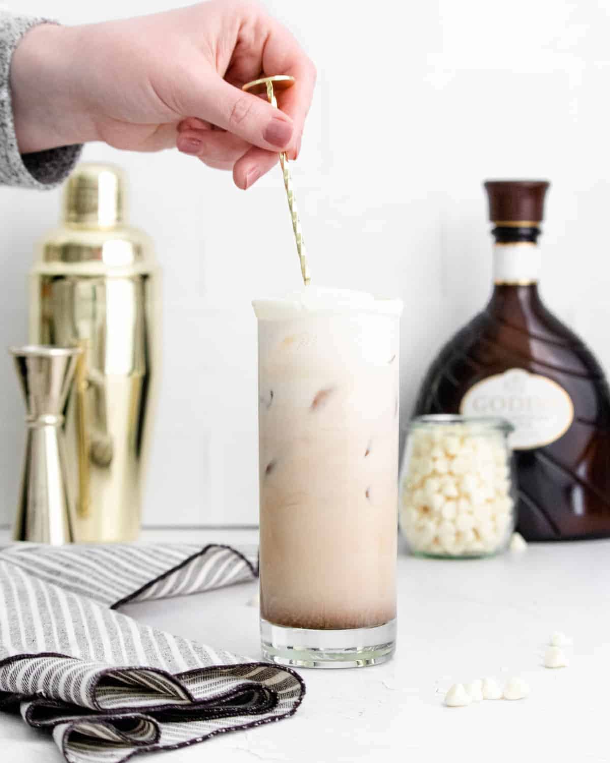 Tall iced white russian in a clear glass, being stirred.