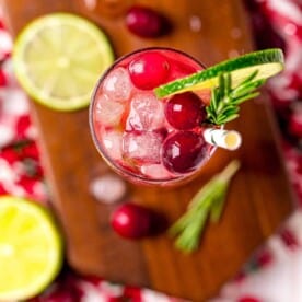 Overhead view of a gin and tonic made with cranberry juice, garnished with fresh cranberries, lime, and rosemary.