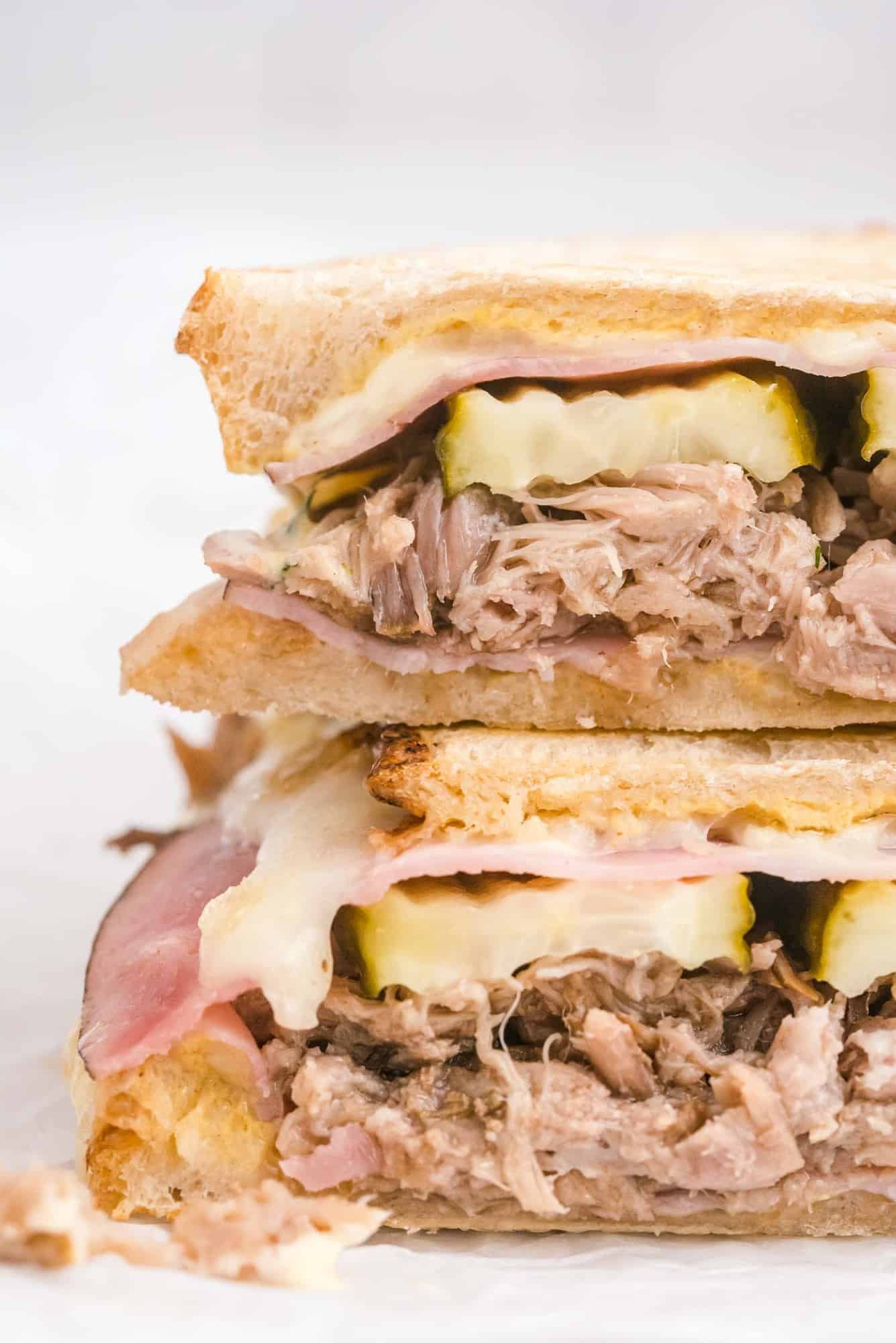 Close up of a sandwich showing layers of pork, pickles, cheese, and ham.