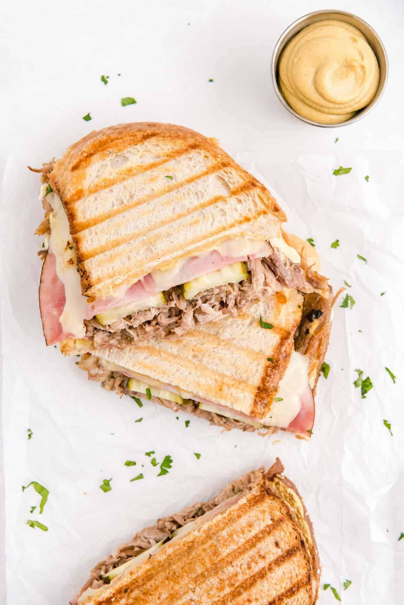 Overhead view of a cuban sandwich, cut in half, with a dish of mustard nearby.