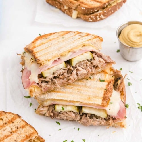 Cuban panini sliced in half, halves stacked on top of each other, on a white surface.