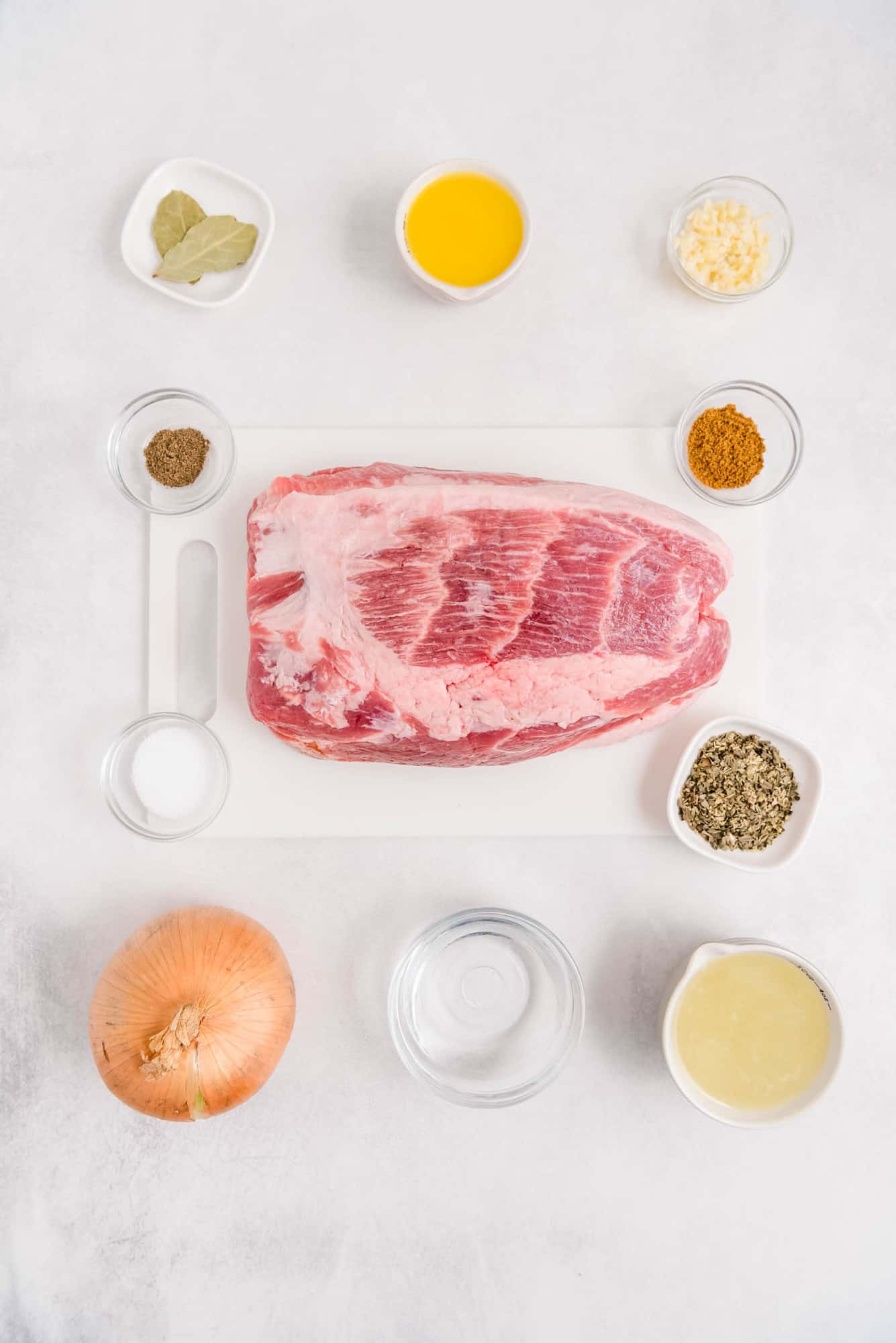 Overhead view of ingredients including pork shoulder, onion, spices, orange juice, and lime juice.