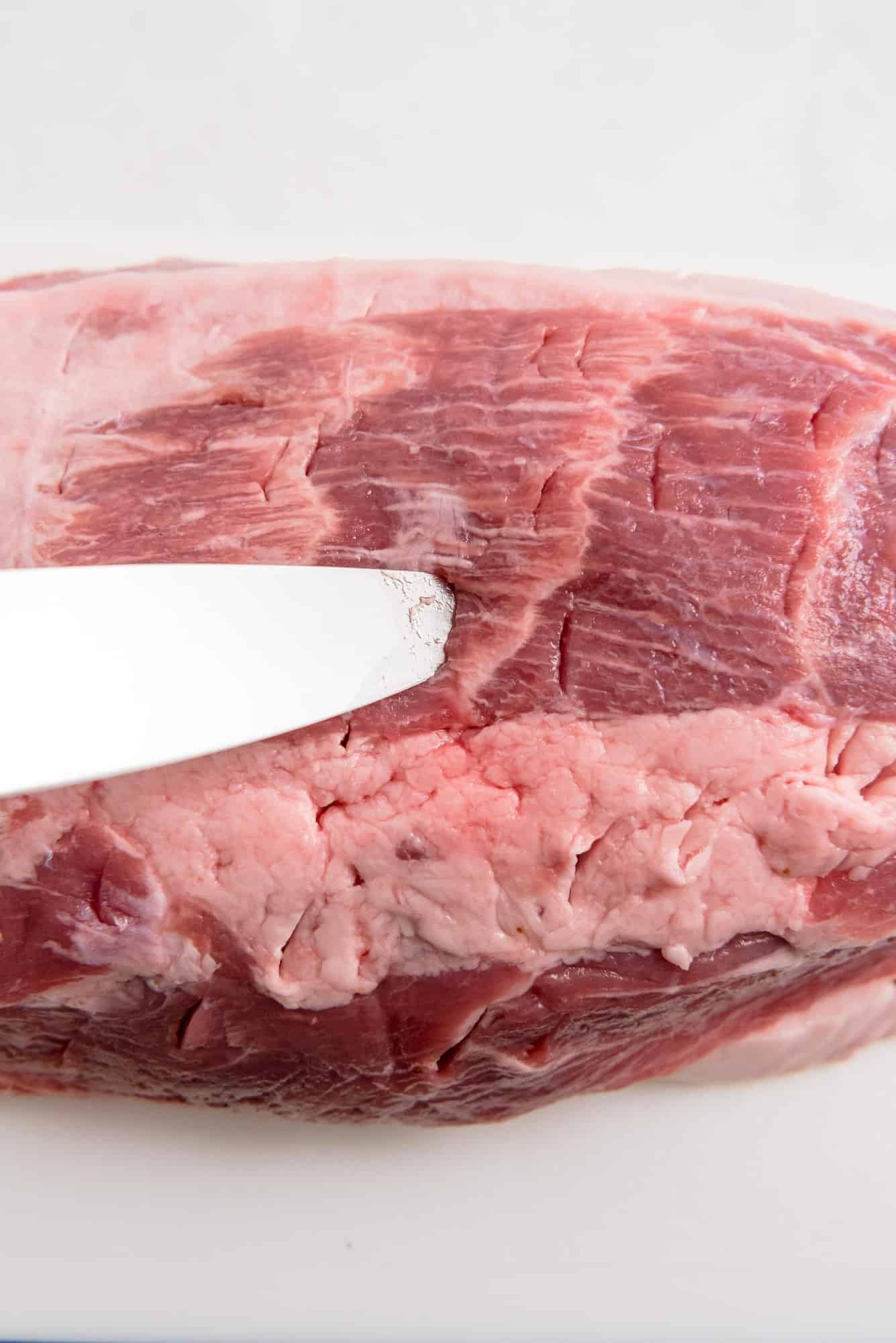 Pork shoulder being cut with a knife.