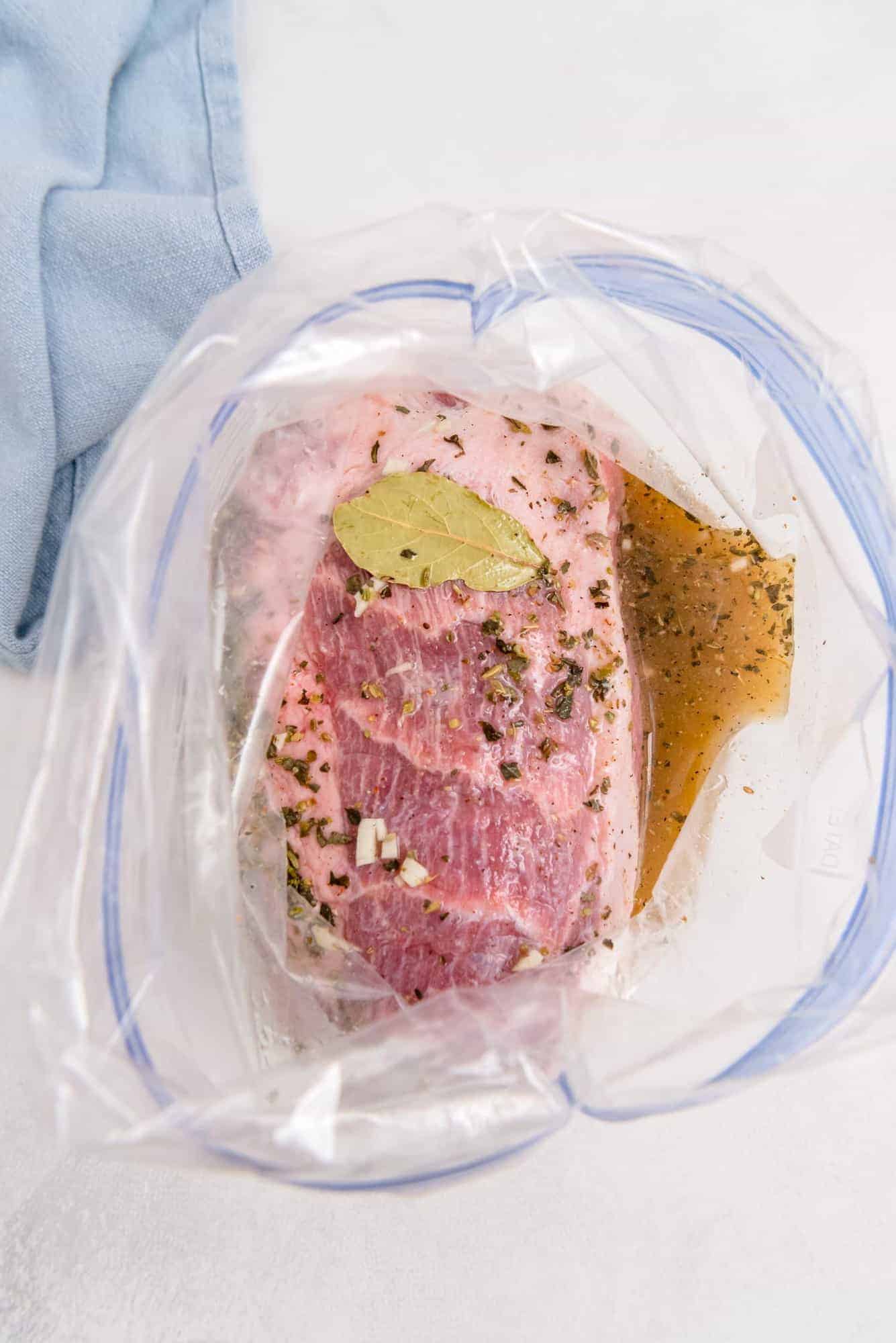 Pork and marinade in a zip-top bag, including a bay leaf.