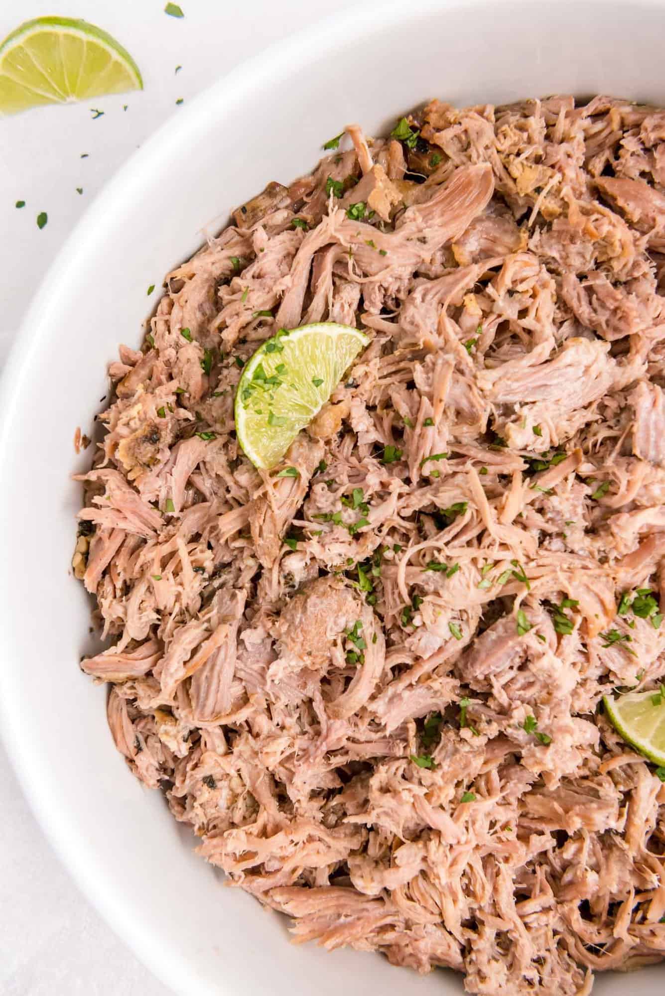 Large white dish of cuban pork garnished with lime wedges.