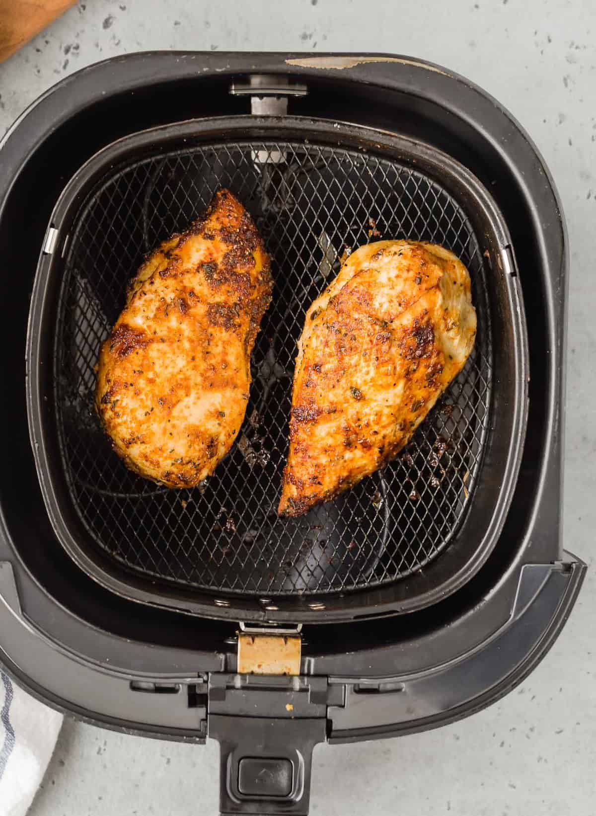 Two chicken breasts in an air fryer basket, overhead view.