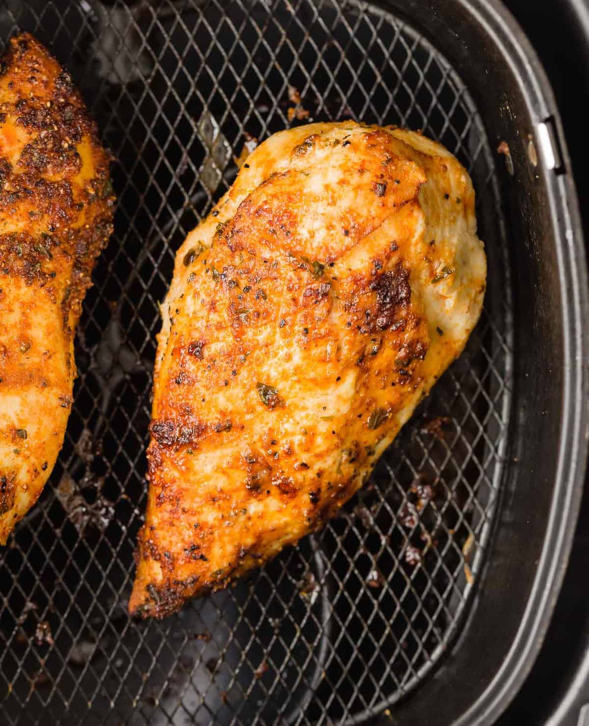 Overhead view of a cooked chicken breast in a black air fryer basket.