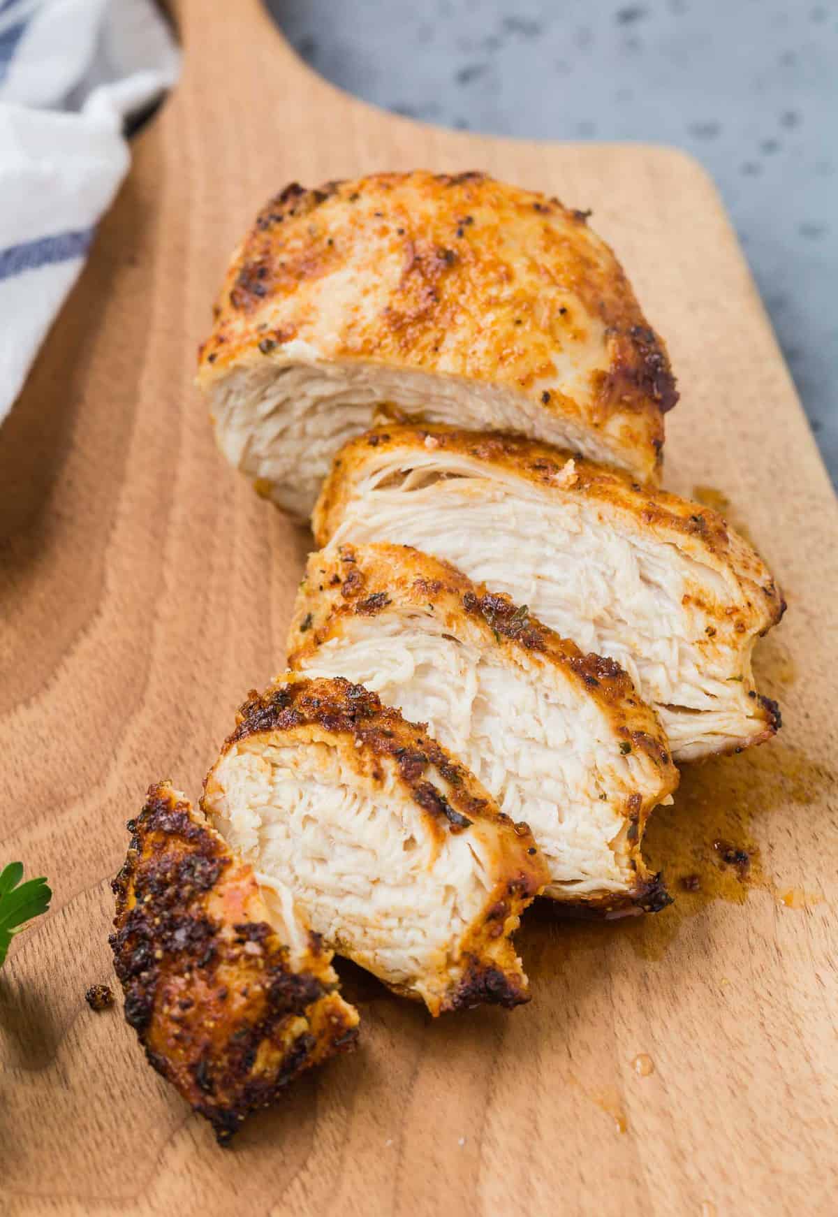 Cut cooked and seasoned chicken breast on a cutting board.