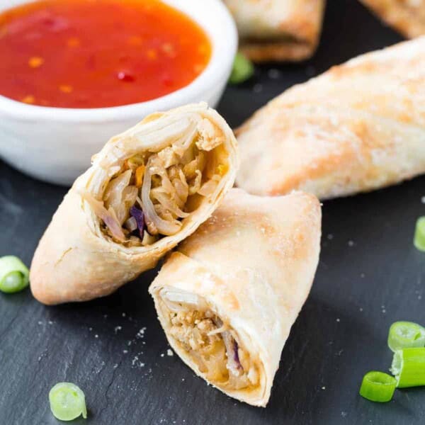 Cut open egg roll on black surface, dipping sauce in background.