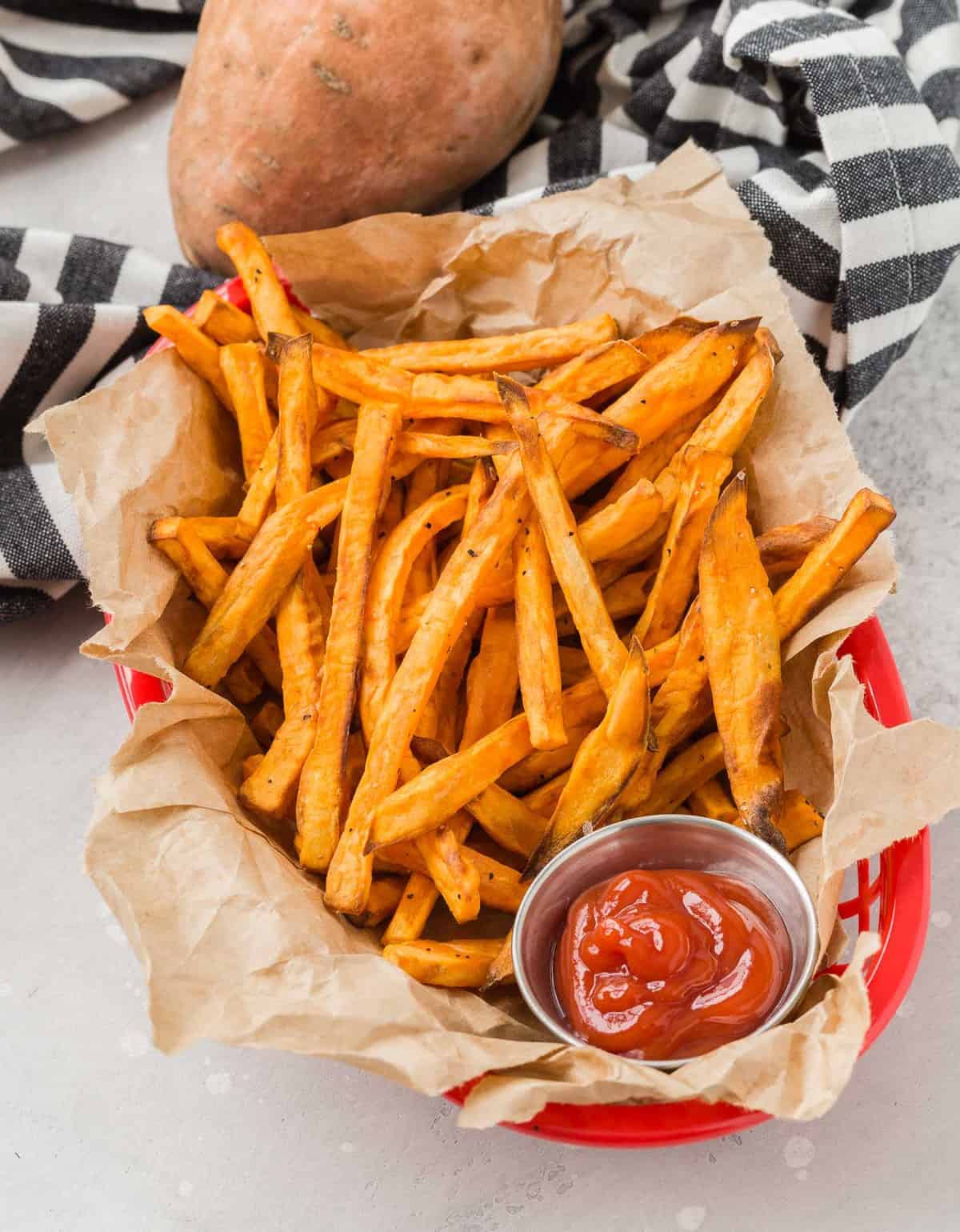 Fries in a basket with ketchup, a sweet potato in the background.