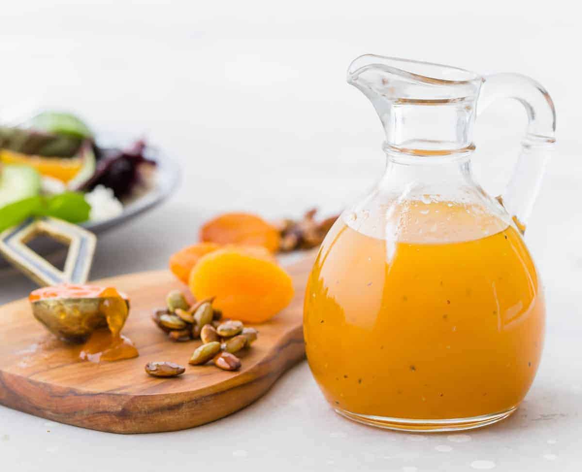 Dressing in a small glass jar next to a small cutting board with apricots.