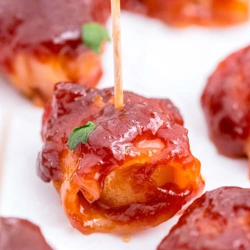 Close up of a water chestnut that is wrapped in bacon and covered in sauce.