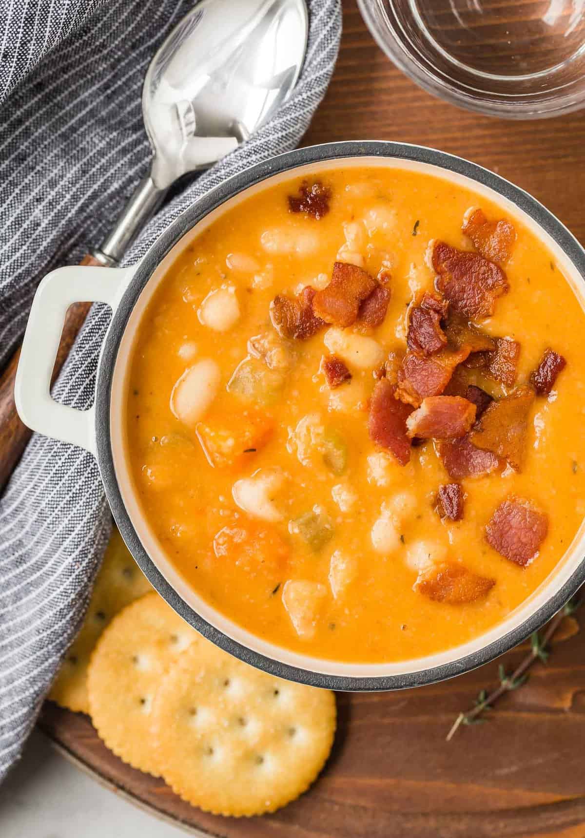 Bean soup topped with bacon in a white bowl with handles.