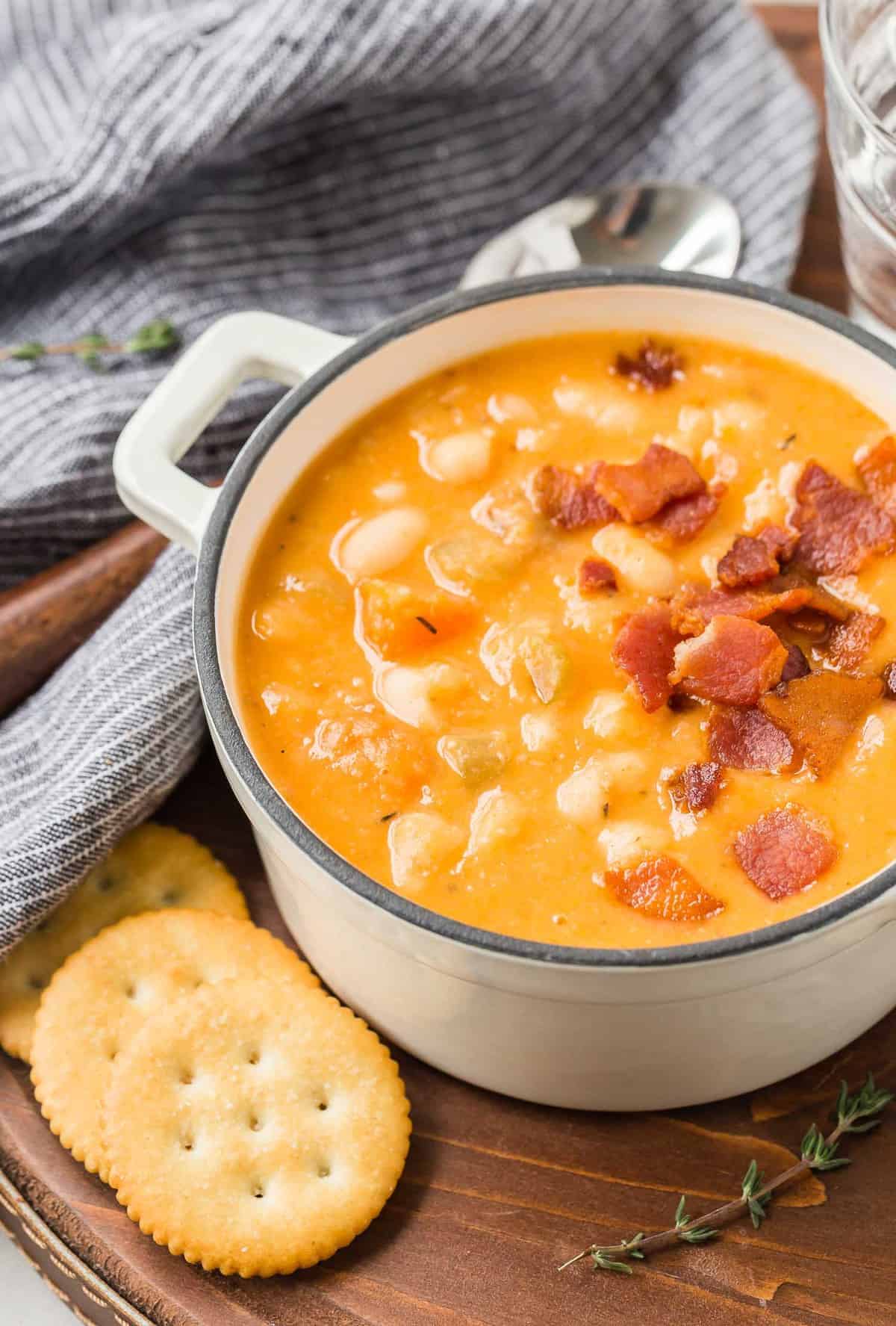 Soup in a white bowl on a wooden tray with crackers and fresh thyme.