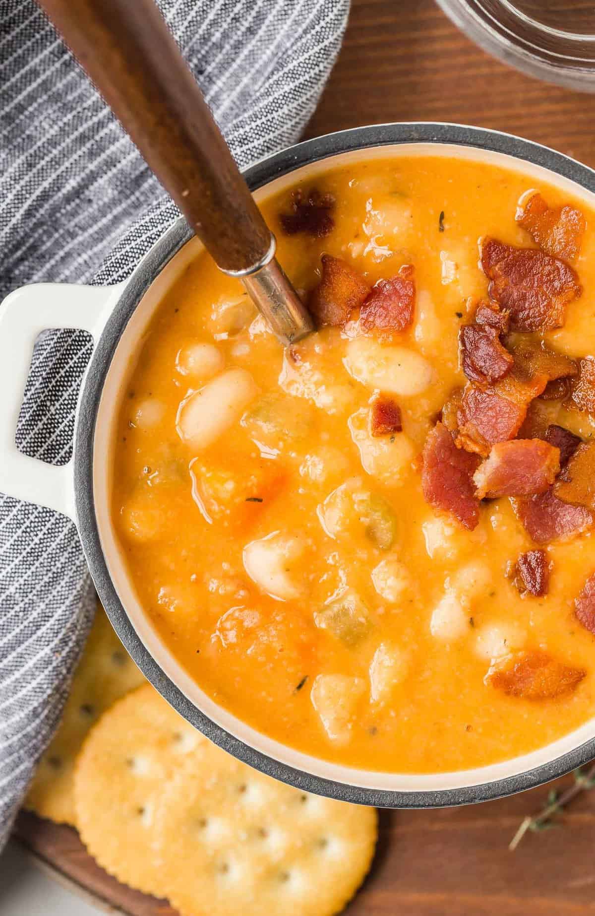 Bean soup, garnished with bacon, with a wooden handled spoon. Ritz crackers also visible.