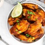 Glazed wings in a white dish with lime wedges.