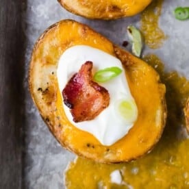 Overhead view of a slice of cooked potato topped with cheddar cheese, sour cream, bacon, and green onion.