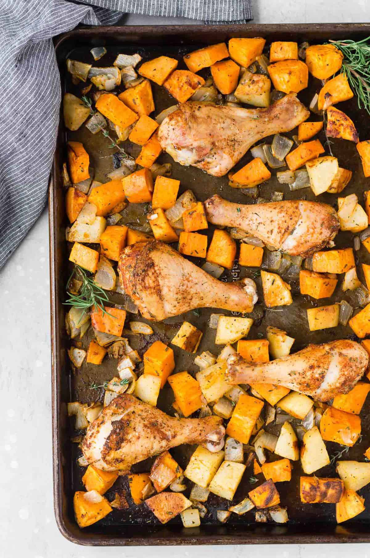 Overhead view of a sheet pan full of roasted potatoes, sweet potatoes, onions, and spice-rubbed drumsticks.