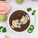 Overhead view of a bowl of black bean soup garnished with lime slices and jalapeno.