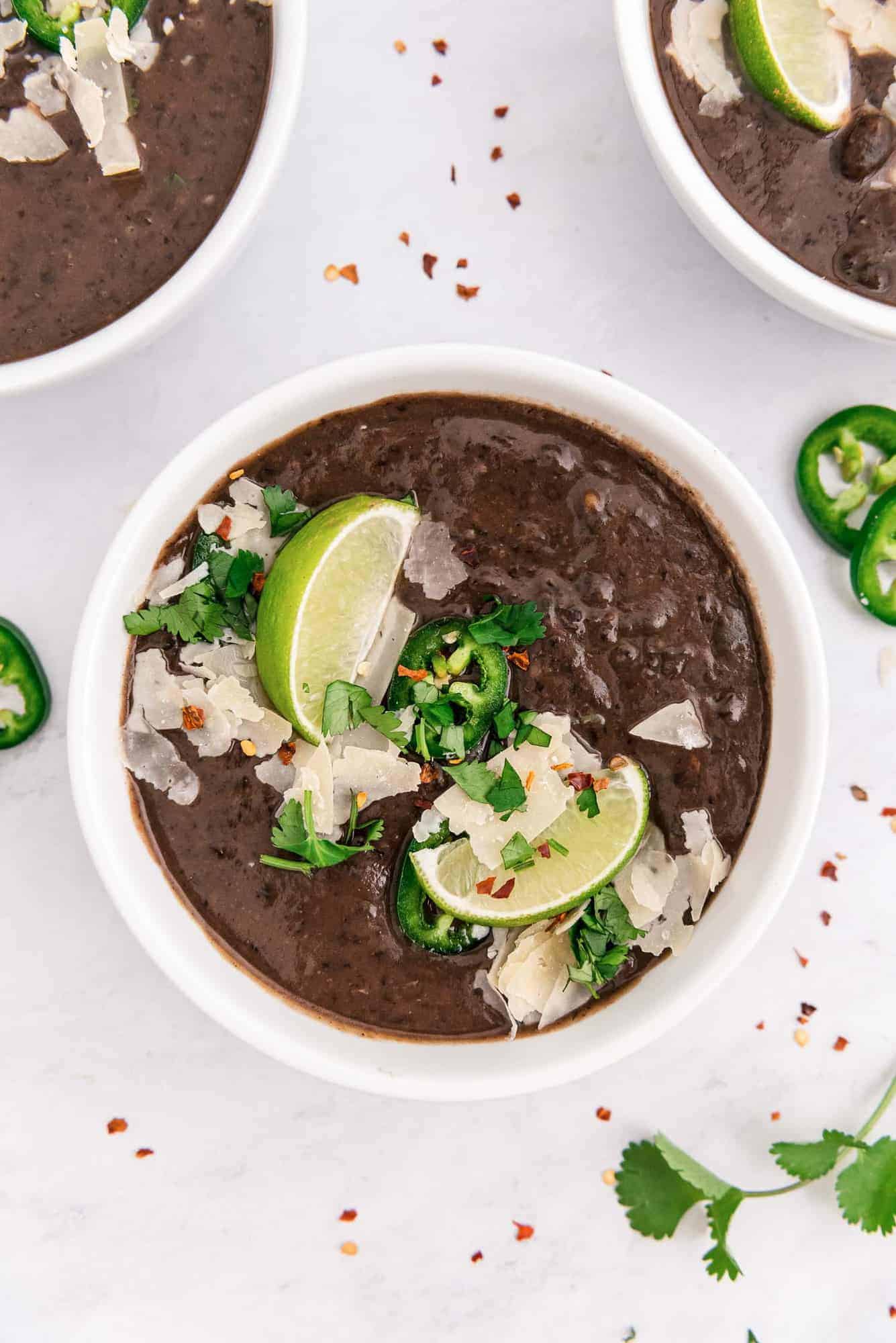 Overhead view of a bowl of black bean soup with garnishes including lime wedges.