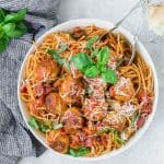 Overhead view of large white bowl full of spaghetti and meatballs, garnished with fresh basil.