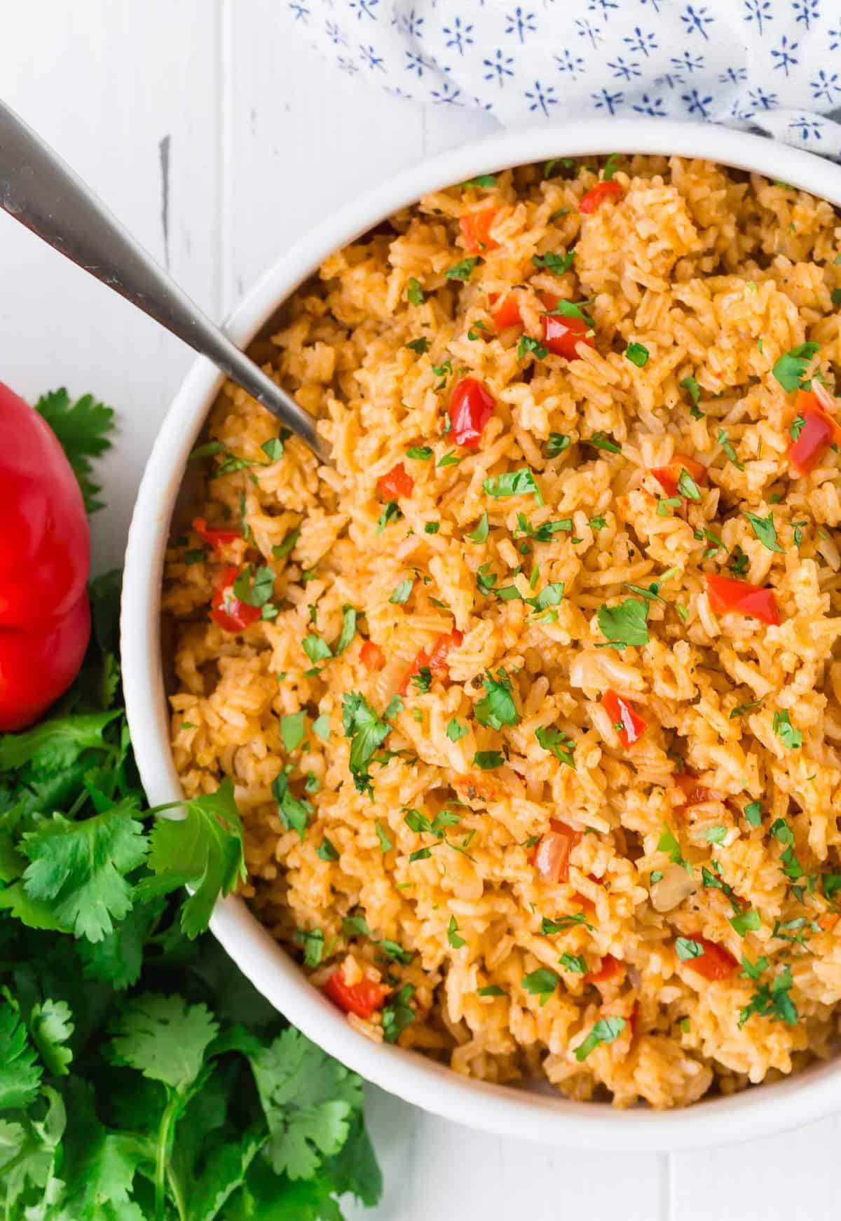 Overhead view of red colored rice in a white serving bowl. Fresh cilantro also visible.