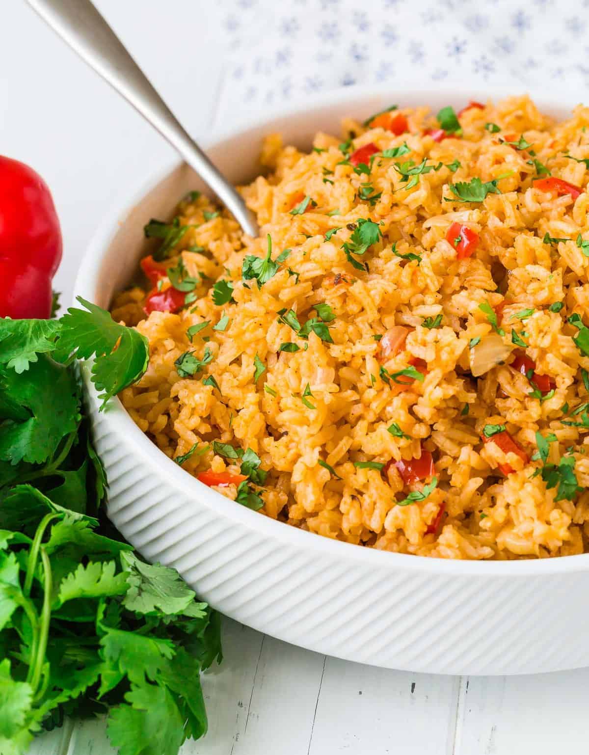 Mexican rice in a white bowl with a silver serving spoon.