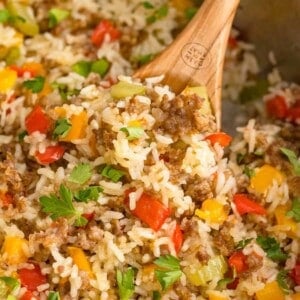 Close up of sausage, rice, and bell peppers in a skillet with a wooden spoon.