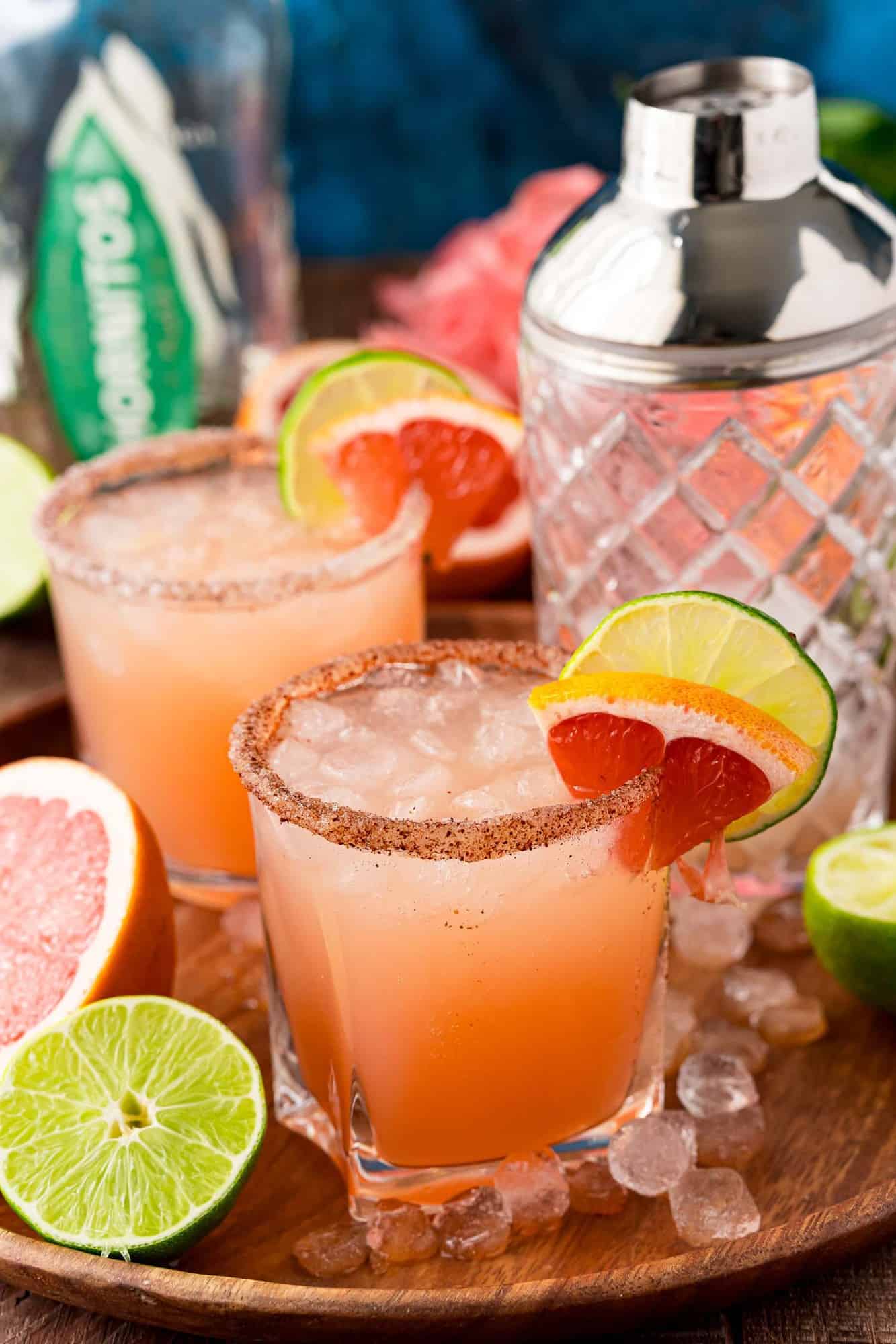 Two light pink cocktails on ice, garnished with grapefruit and lime.