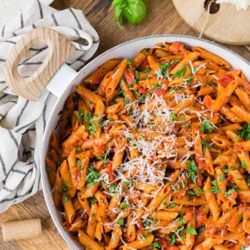 Overhead view of a pan of pasta with tomato sauce, fresh parsley, and grated cheese.