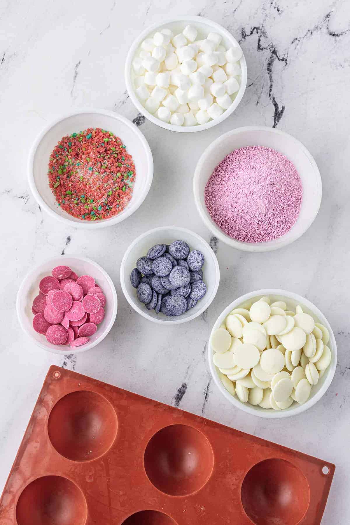 Overhead view of ingredients needed to make hot chocolate bombs, candy melts, pop rocks, and marshmallows are included.