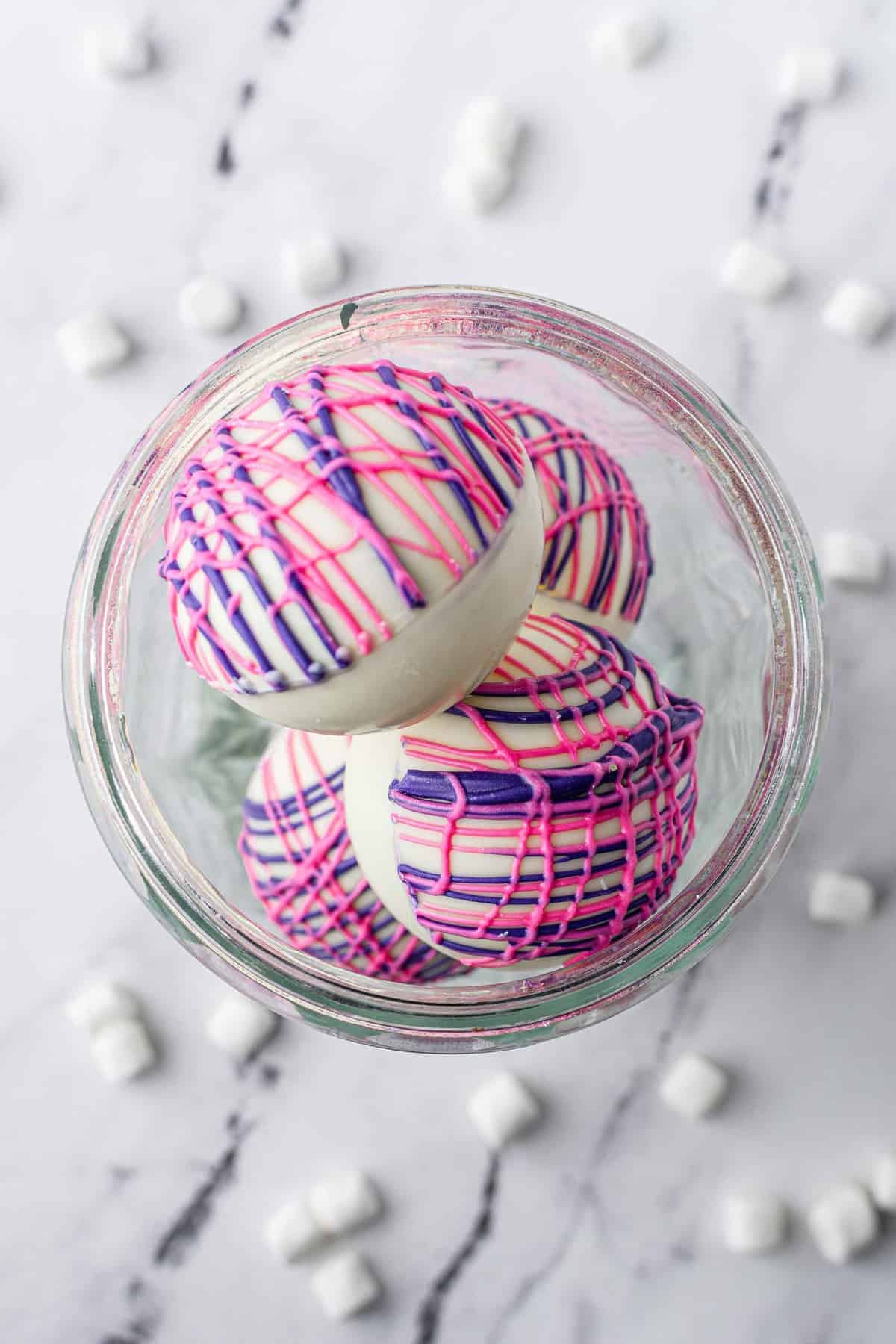 Overhead view of colorful hot cocoa bombs in a glass container.