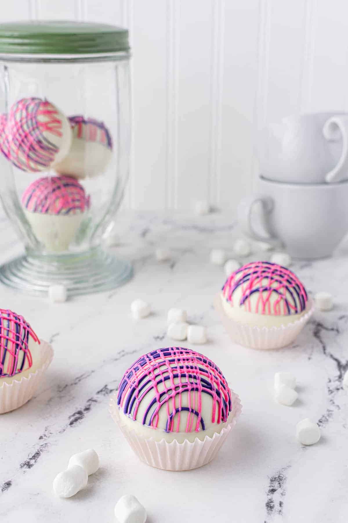 Pink, white, and purple chocolate spheres in the foreground, jar of more in the background.