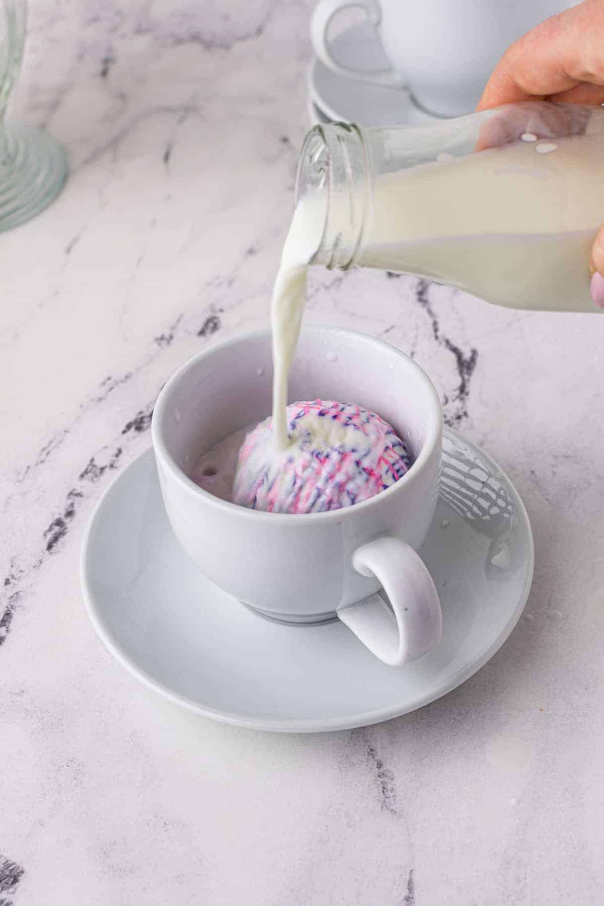 Milk being poured over a white chocolate hot cocoa bomb.