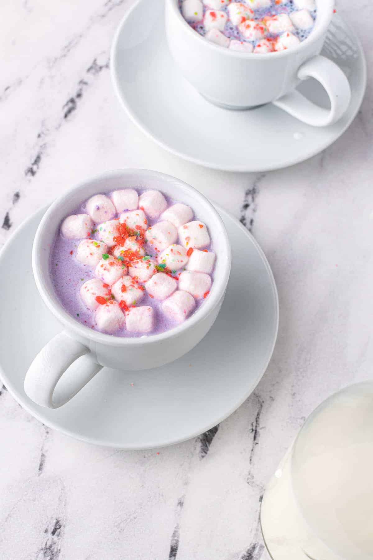 Overhead view of a white mug with a purple colored beverage and marshmallows.
