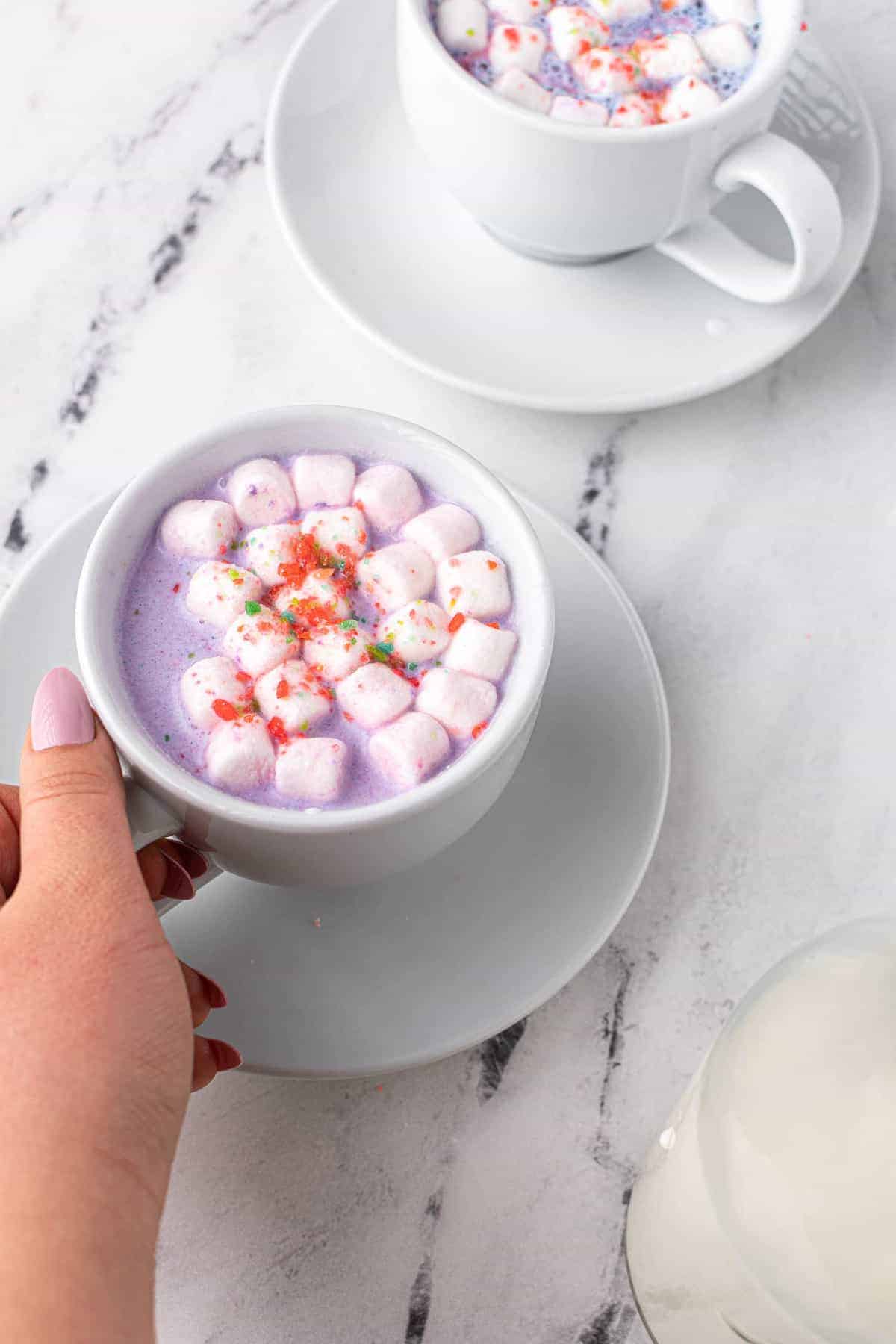 Mug of purple cocoa with marshmallows, hand holding handle of mug.